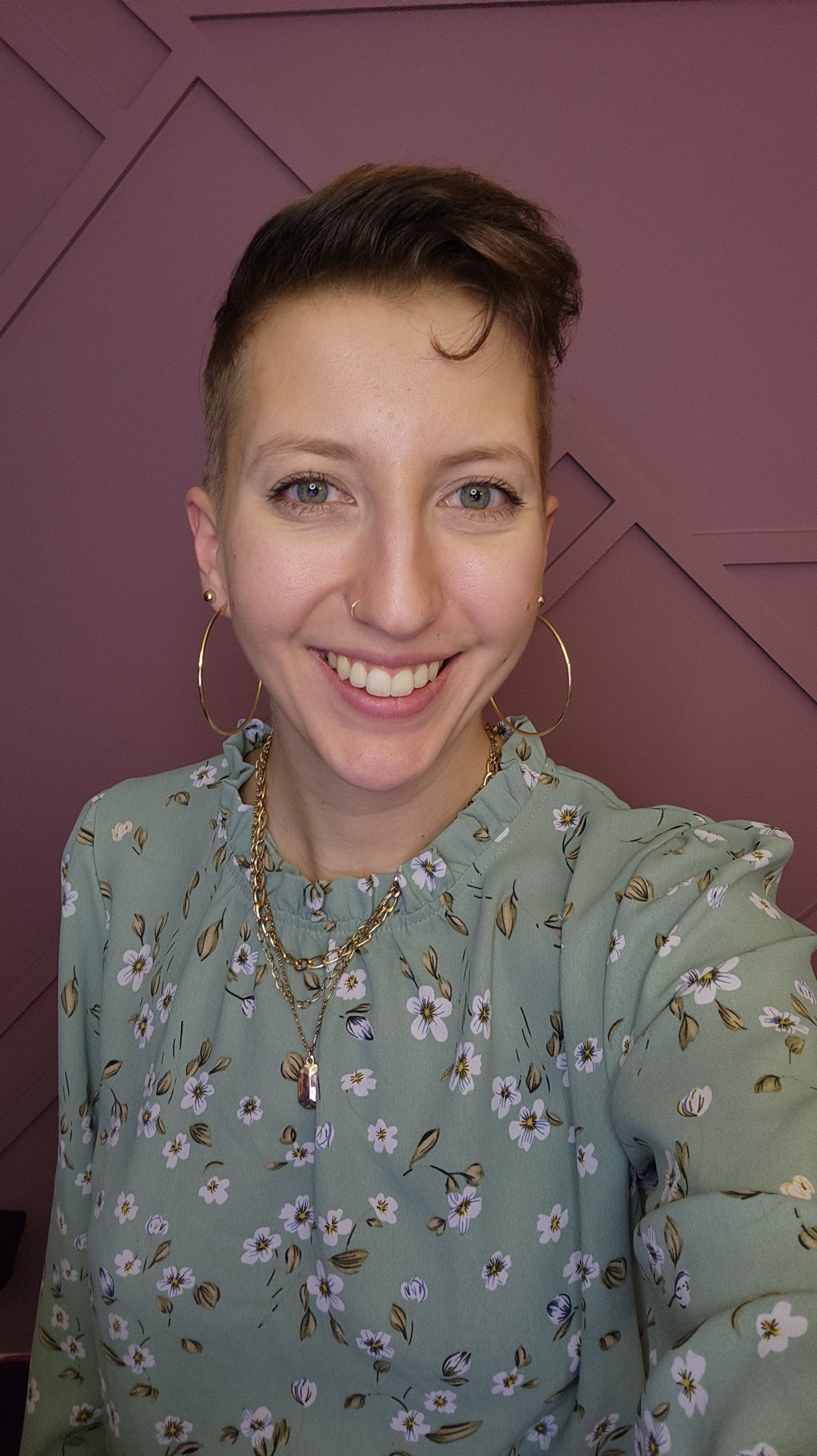 Cameron smiling in her green floral blouse in front of a purple background