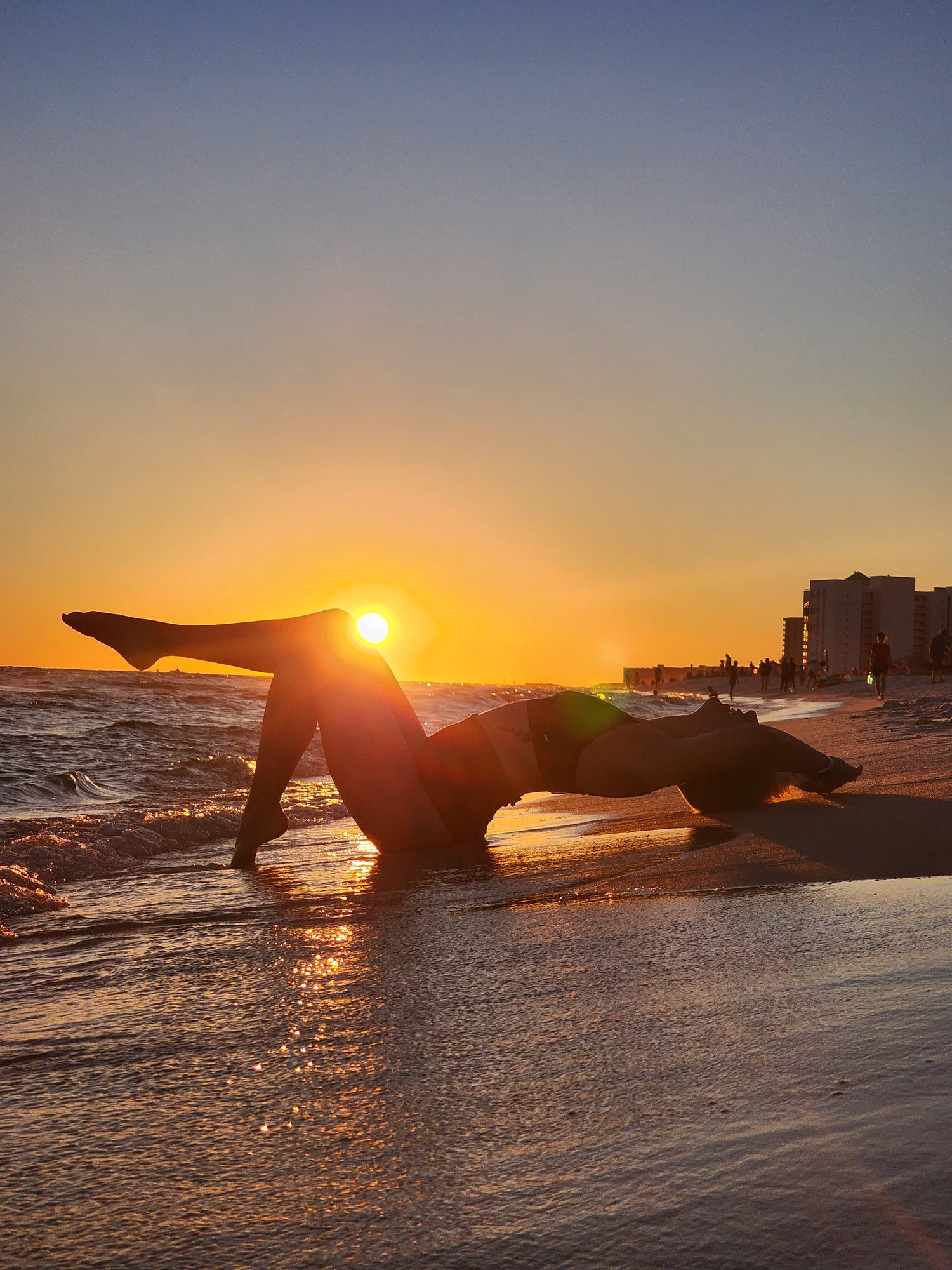 Cameron on the beach with the sun by her knee at sunset